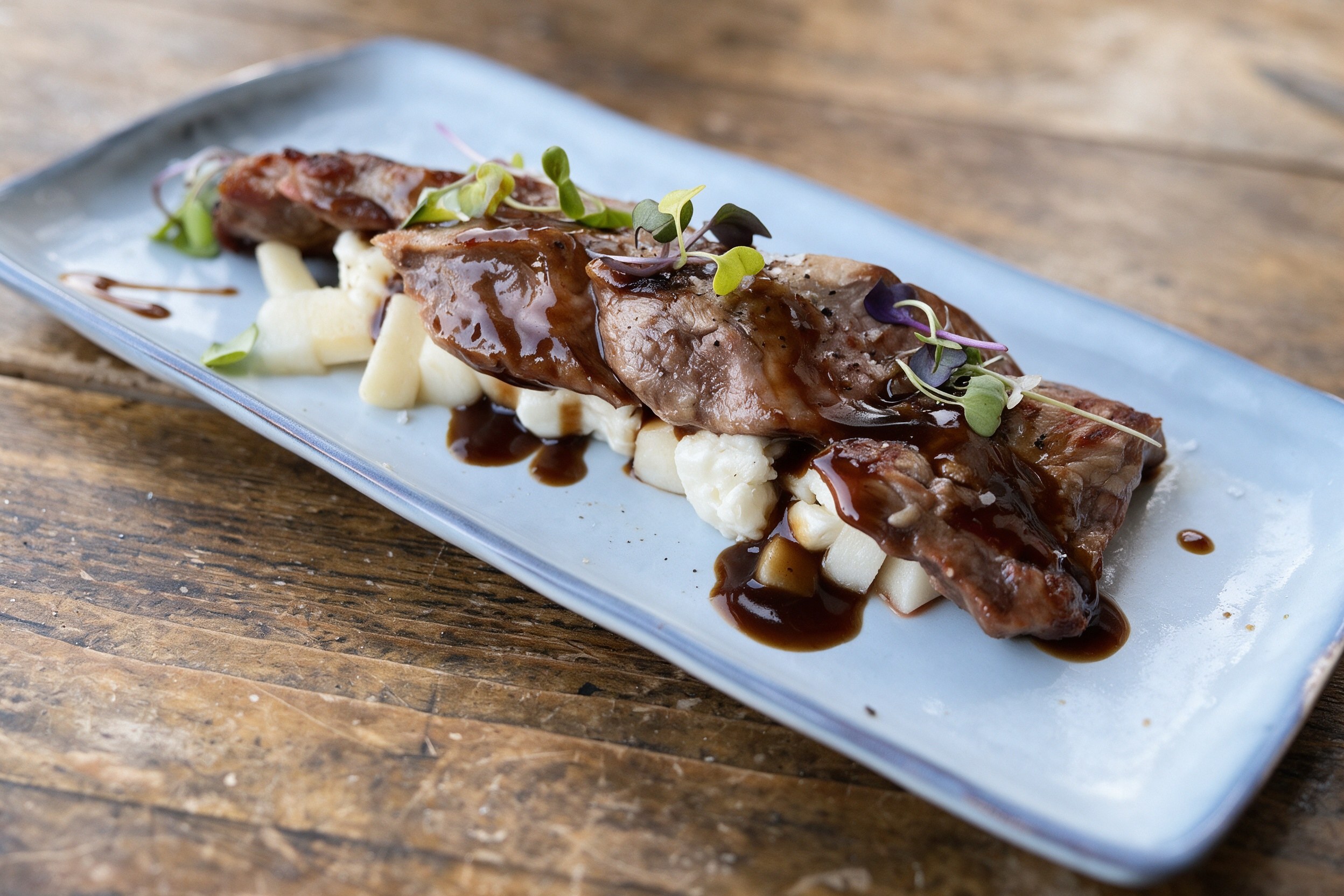 Medallones de carne a la brasa con glaseado balsámico y virutas sobre plato blanco