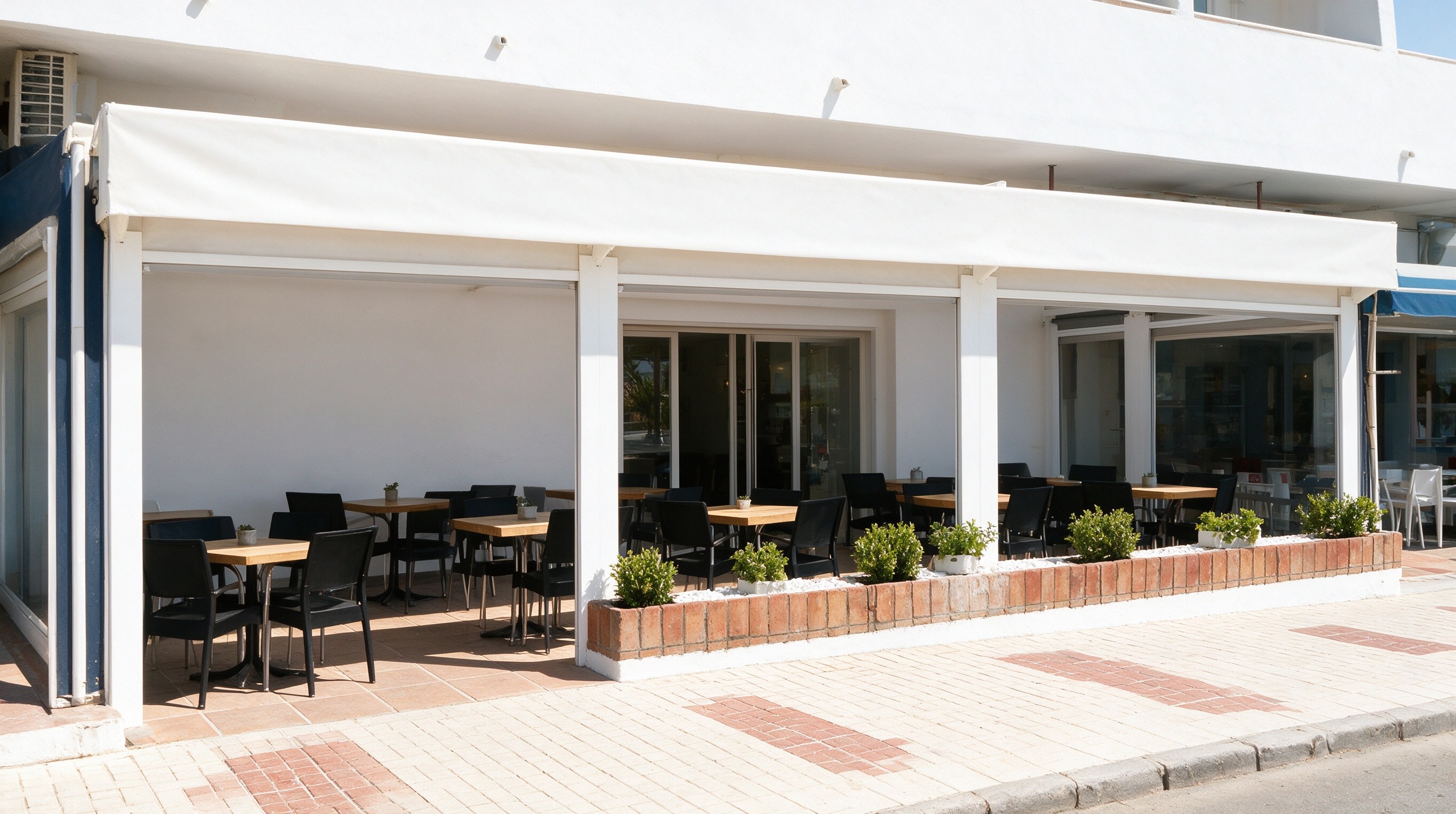 Fachada blanca de gastrobar con terraza de madera y macetas junto a una calle peatonal soleada